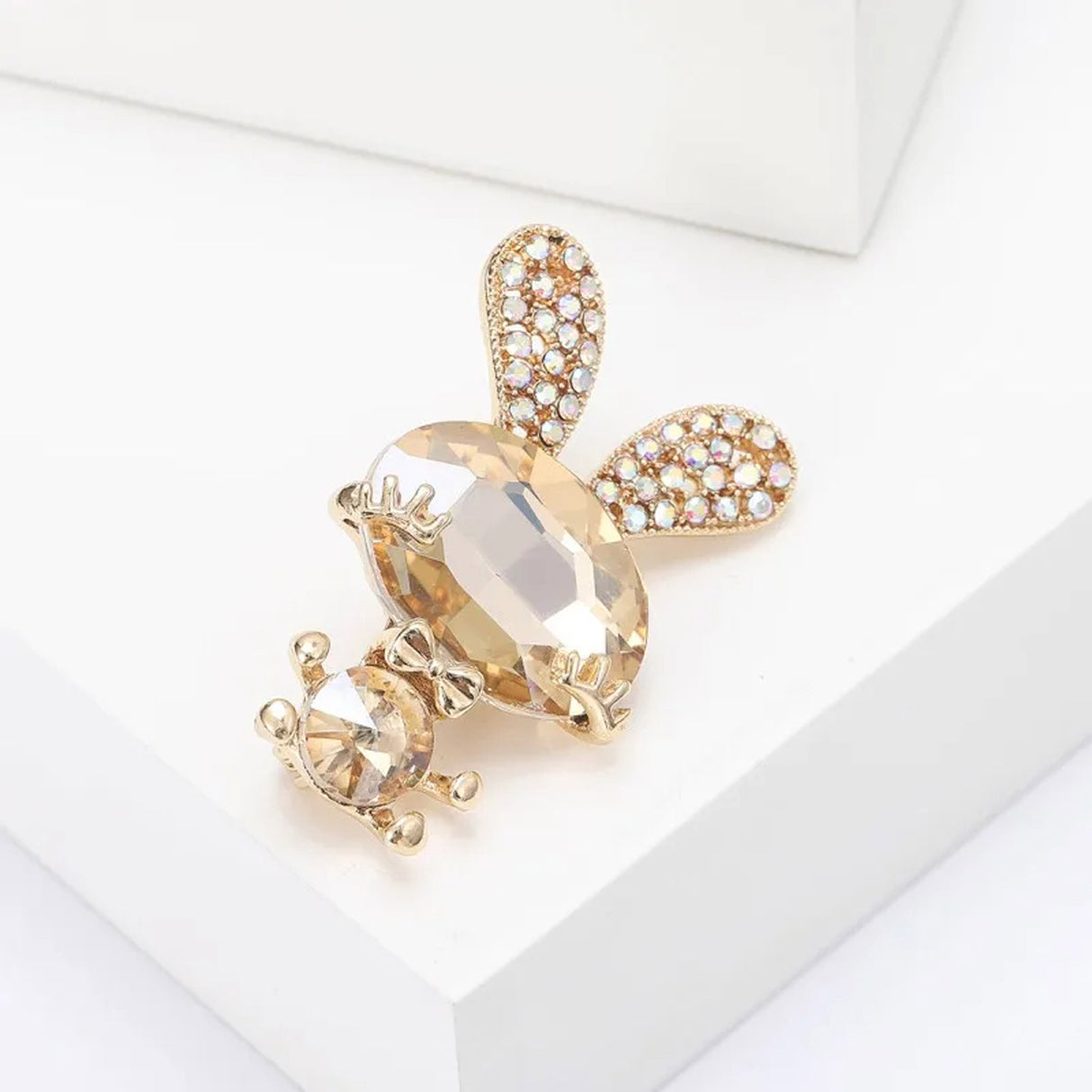 Bunny brooch with amber-yellow faceted stones, gold arms and feet, and crystal studded ears, angled view on white studio platform.