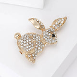 Bunny brooch with gold-tone metal, clear faceted stones, and black eye, angled view on white surface.