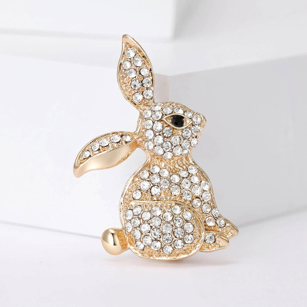Bunny brooch in gold-tone finish with clear faceted stones and black eye detail, standing pose on white background.