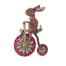 Bunny brooch with pink rhinestone pave, riding a bicycle with clear and magenta stone wheels. Cutout on white background.