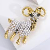 Ram brooch with gold-tone finish, white round bead body, and clear faceted stones on the face, angled side view.