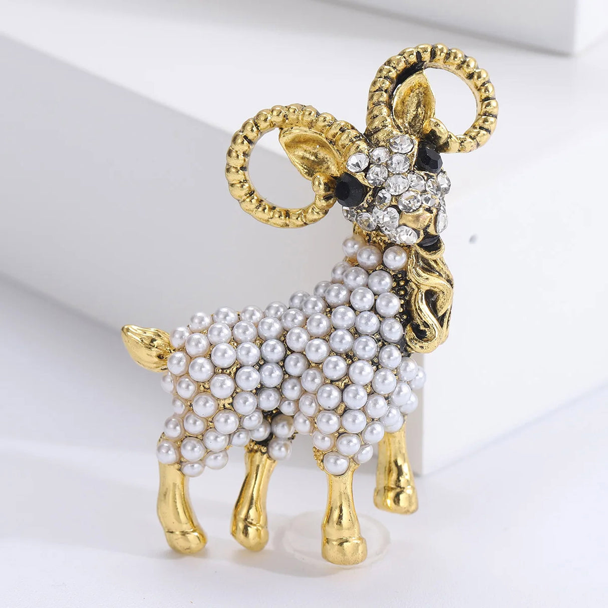 Ram brooch in gold-tone metal with clustered white faux pearls and clear stones on face, upright studio pose.