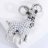 Ram brooch with silver-tone finish, white round bead body, and clear decorative stones on head, angled top view on white.