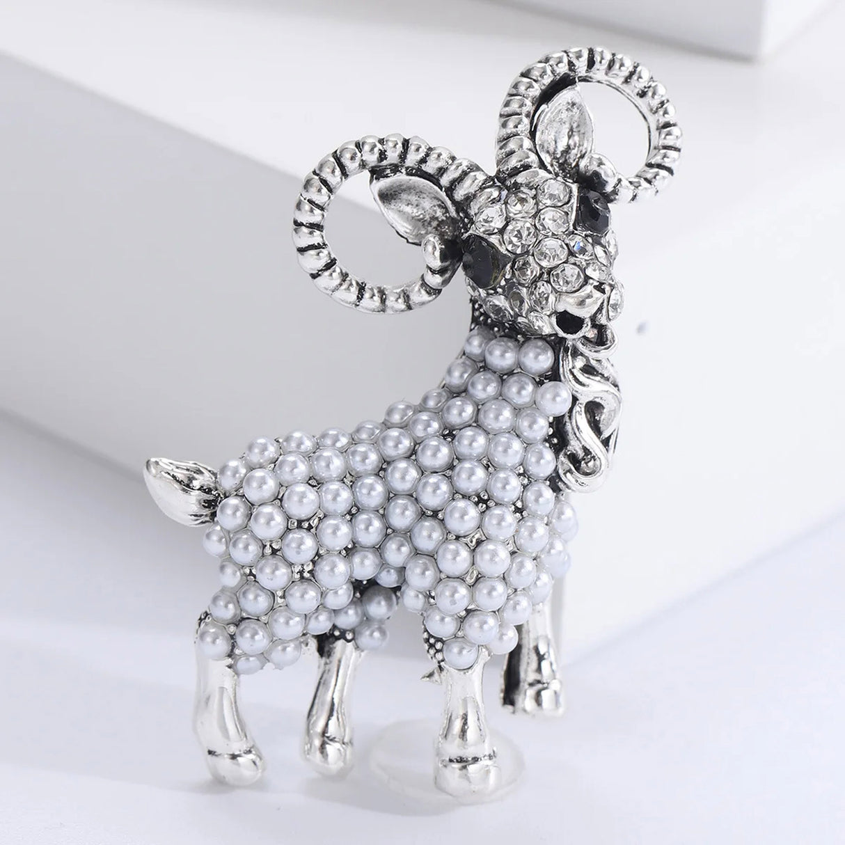 Ram brooch in silver-tone metal with clear stones on face and white imitation-pearl body, standing front pose.