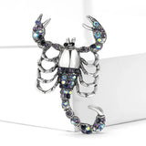 Scorpion brooch with silver-tone base, iridescent blue-purple stones, and curled tail, upright view on white block.