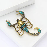 Scorpion brooch with gold-tone base, teal and clear stones, angled flat lay on white surface.