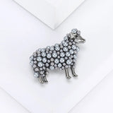 Sheep brooch with grey-tone metal and layered beads, angled top view on white platform.