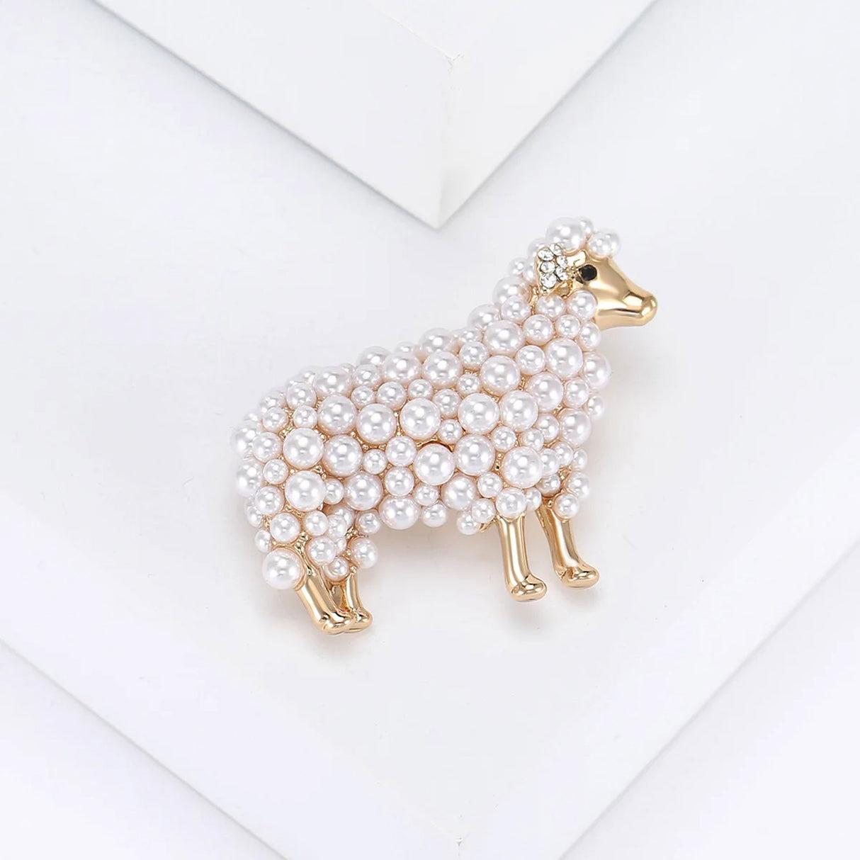 Sheep brooch with gold-tone finish, clustered white round beads, and clear ear stones, angled view on white surface.