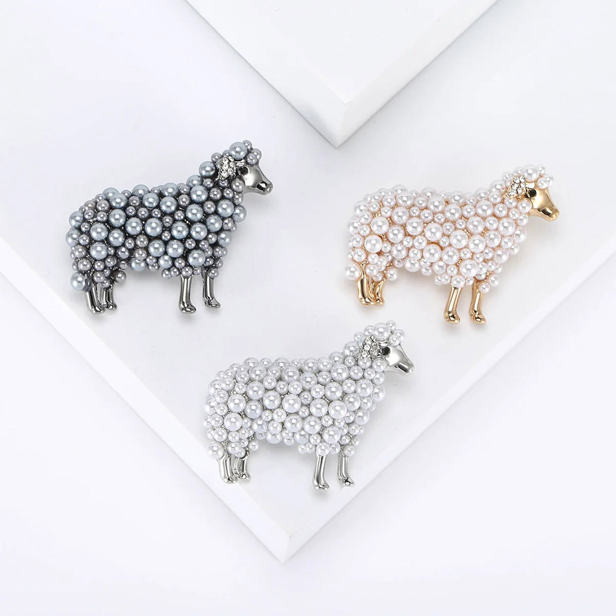 Set of three sheep brooches in grey-tone, gold-tone, and silver-tone finishes with round beads, flat lay on white platform.