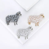 Set of three sheep brooches in grey-tone, gold-tone, and silver-tone finishes with round beads, flat lay on white platform.