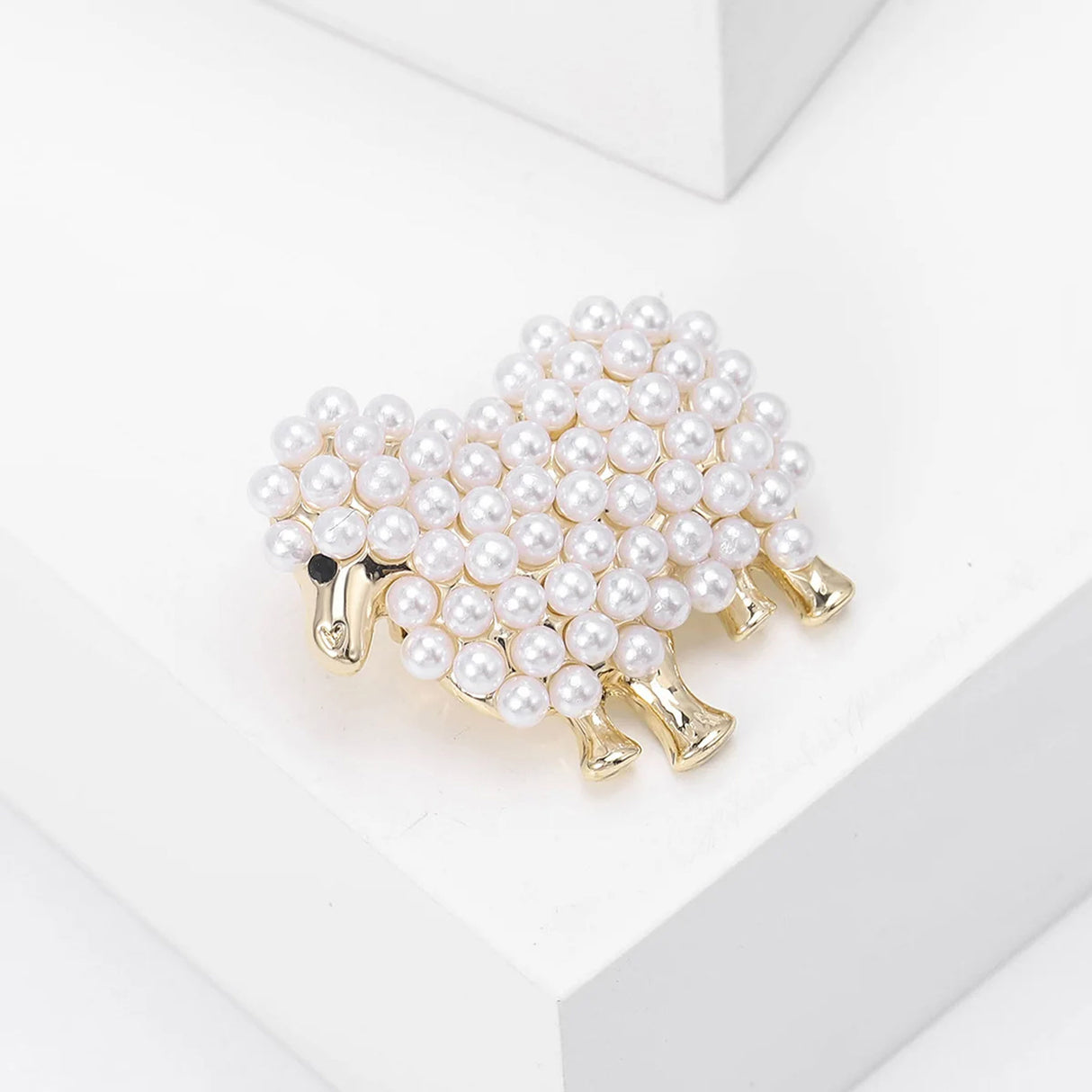 Sheep brooch with gold-tone metal finish and clustered white faux pearls forming the body, angled top view on white block.