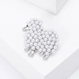 Sheep brooch in silver-tone metal with white round beads and black eye detail, angled top view on white studio surface.