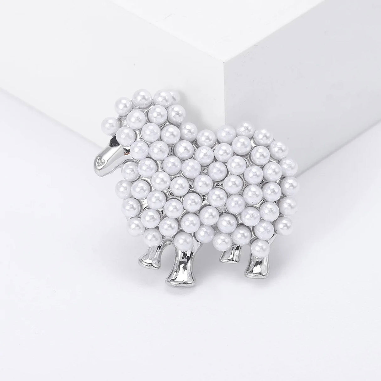 Sheep brooch with silver-tone metal finish and white imitation pearls forming a textured body, displayed on white block in studio.