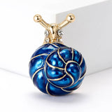 Snail brooch featuring blue-toned spiral shell, gold-tone body, and clear stones, upright view on white studio backdrop.