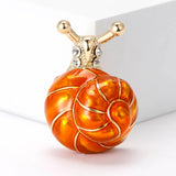 Snail brooch with orange-toned swirl shell, gold-tone metal and clear stones, upright studio view on white.