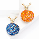 Pair of snail brooches with blue and orange-toned spiral shells, gold-tone bodies and clear stones, flat lay on white.