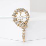 Snake brooch with gold-tone base, clear faceted stones, and a hanging clear teardrop stone, upright on white block.