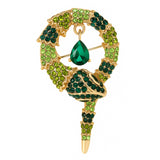 Snake brooch with gold-tone metal base, faceted stones in dark and light green tones, and green teardrop pendant, cutout on white.