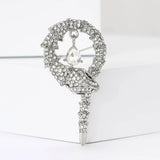 Snake brooch with silver-tone base, clear faceted stones, and a hanging clear teardrop stone, upright on white block.