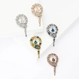 Set of five snake brooches in blue, green, red, silver, and gold-tone variations with hanging teardrop stones, flat lay on white surface.