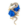 Snake brooch with clear pave stones and green eyes, set in gold-tone metal base, with vivid blue rose accents. Cutout on white background.