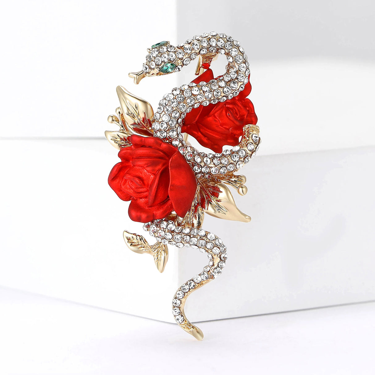 Snake brooch adorned with clear pave-set stones, gold-tone leaves, and two red rose motifs. Upright pose on white studio background.