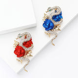 Pair of snake brooches in gold-tone metal, with red and blue roses and clear pave-set stones. Top-down view on white studio backdrop.