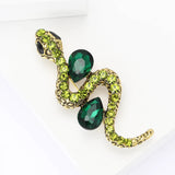 Snake brooch in gold-tone metal with dark green teardrop stones and yellow-green crystals, top-down view on white.