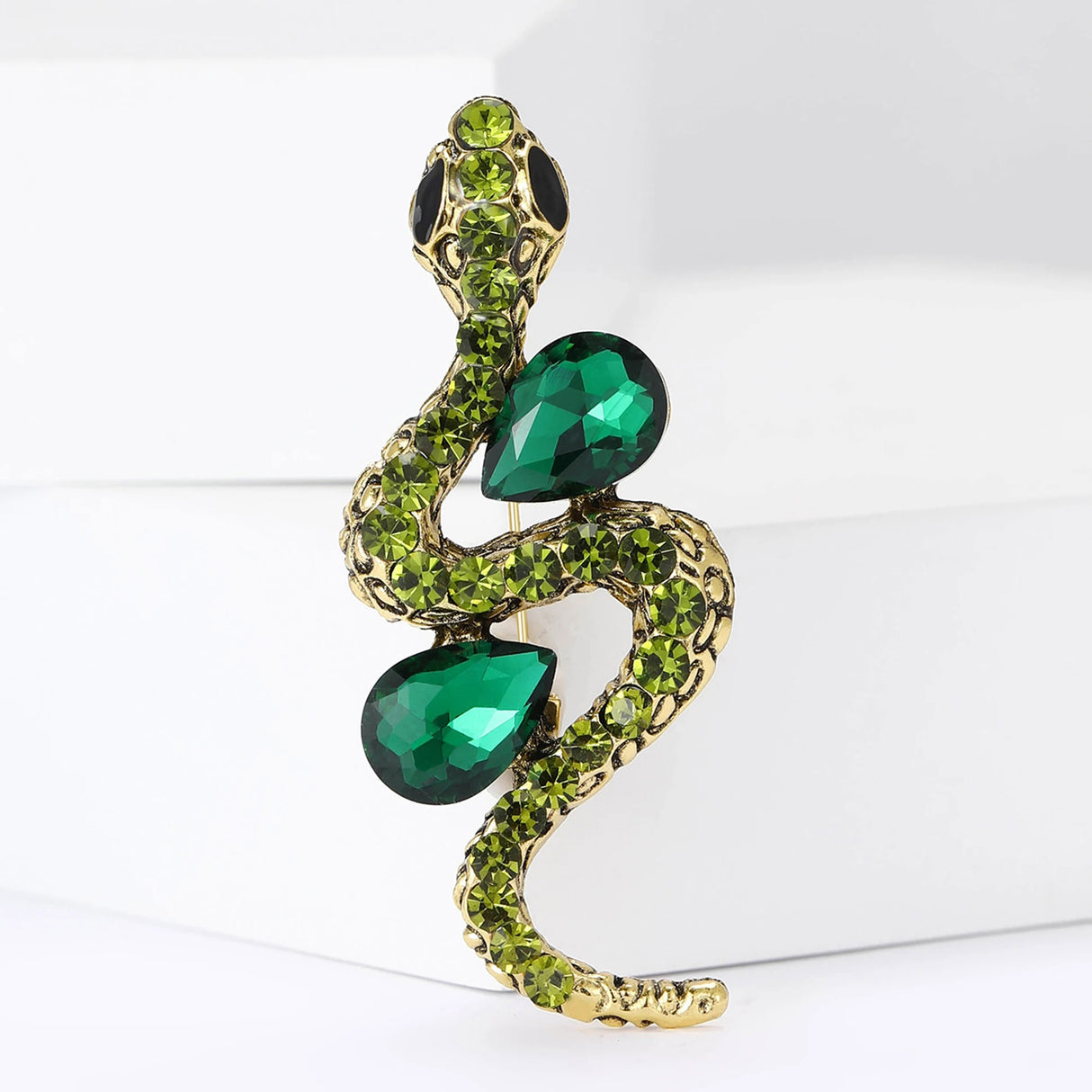 Snake brooch with gold-tone body, emerald-toned teardrop stones, and lime green round crystals, upright view on white.