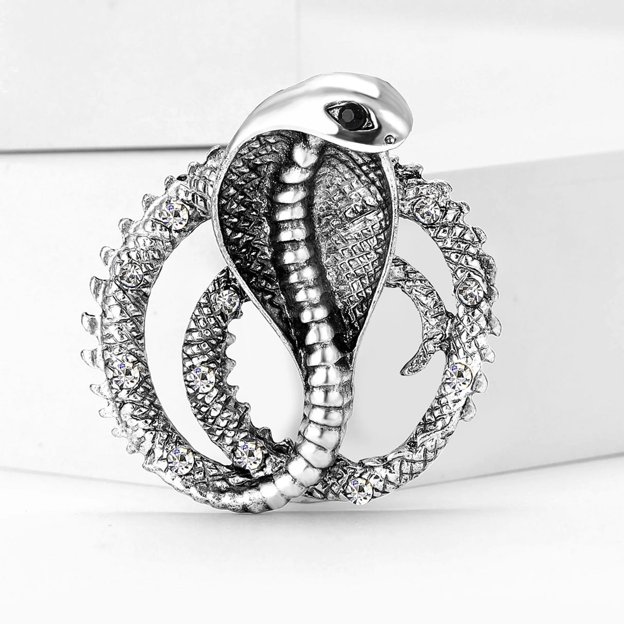 Silver-tone cobra brooch with clear accent stones and textured coiled body, upright on white studio background.