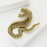 Gold-tone snake brooch with textured scales and small light brown stones, flat lay on white surface.