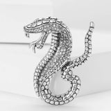 Silver-tone snake brooch with clear faceted stones and textured scale details, upright pose on white block.