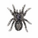 Tarantula brooch with silver-tone base, black and clear faceted stones, and a dark oval cabochon center, cutout on white.
