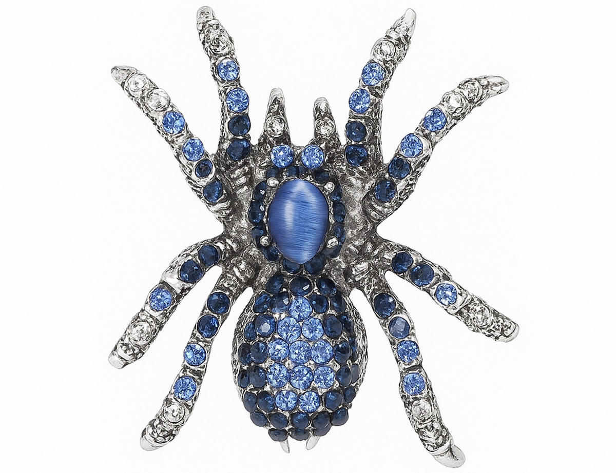 Tarantula brooch with silver-tone base, light and dark blue faceted stones, and a blue oval cabochon center, cutout on white. Landscape crop for secondary use.