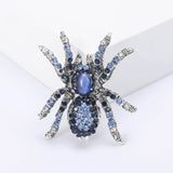 Tarantula brooch with light and dark blue faceted stones and a blue oval cabochon center, upright view on white block.