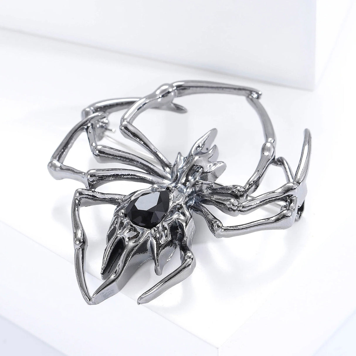 Spider brooch with gunmetal-tone finish and black faceted teardrop stone in the center, angled view on white block.