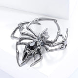 Spider brooch with gunmetal-tone finish and black faceted teardrop stone in the center, angled view on white block.