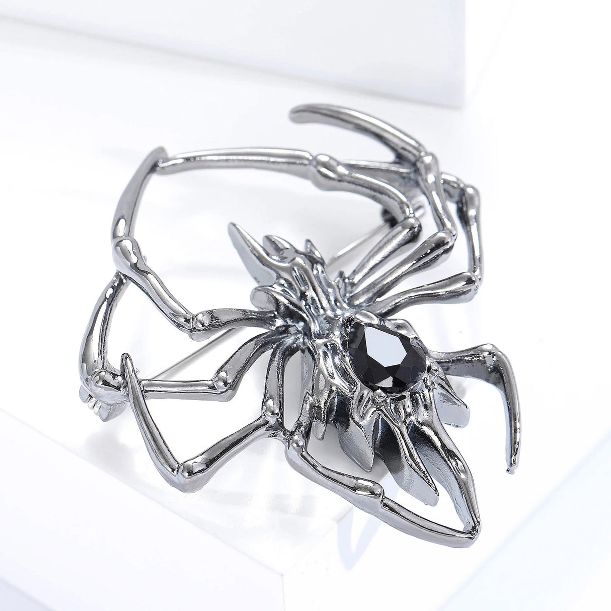Gunmetal-tone spider brooch featuring black teardrop-shaped faceted stone, tilted side angle on white platform.