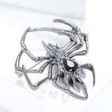 Gunmetal-tone spider brooch featuring black teardrop-shaped faceted stone, tilted side angle on white platform.