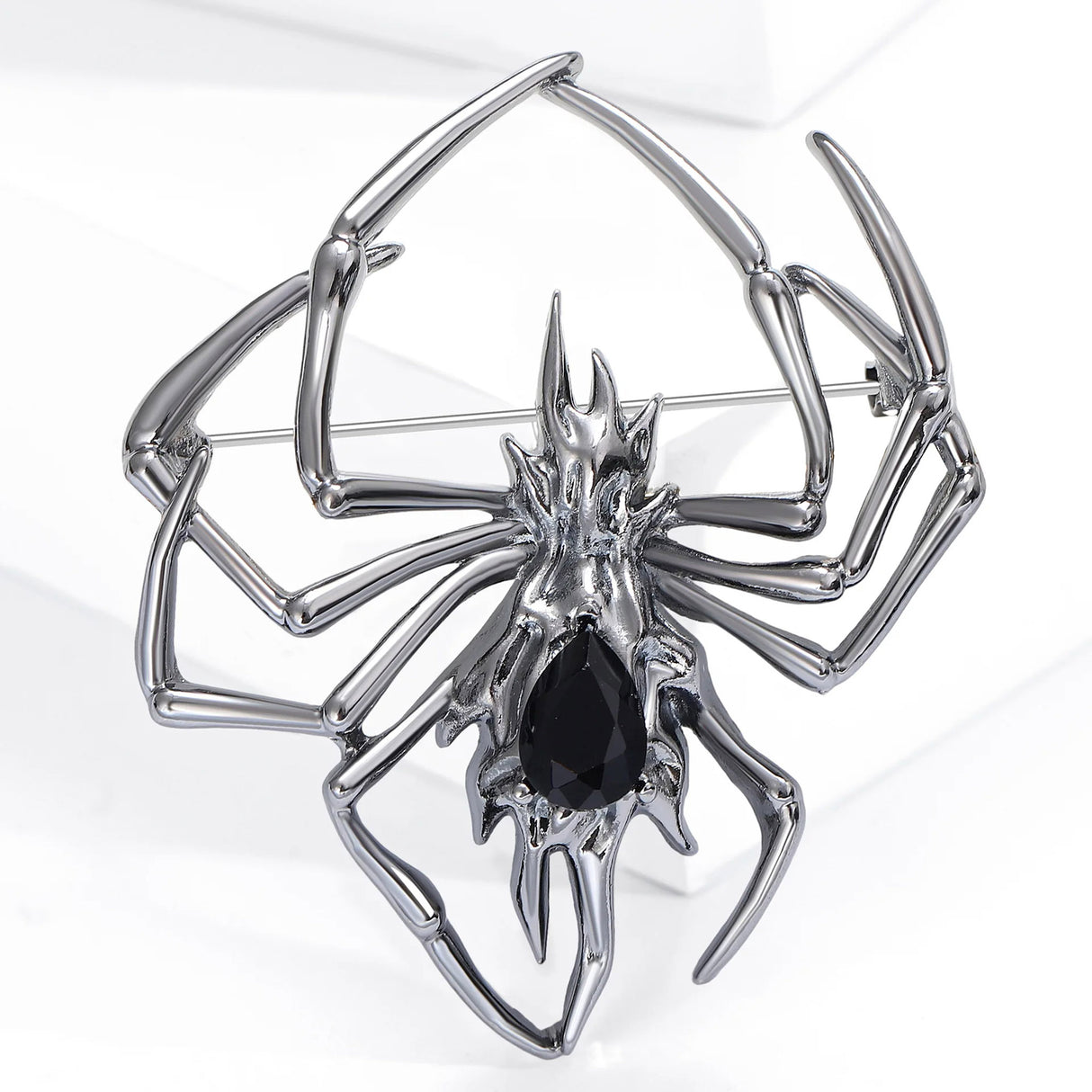 Gunmetal-tone spider brooch with large black teardrop faceted stone, upright on white block.