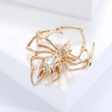 Spider brooch in gold-tone metal finish with clear faceted teardrop center stone, angled pose on white studio background.
