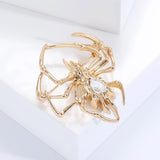 Gold-tone spider brooch with clear teardrop stone and textured legs, side view from top on white block.