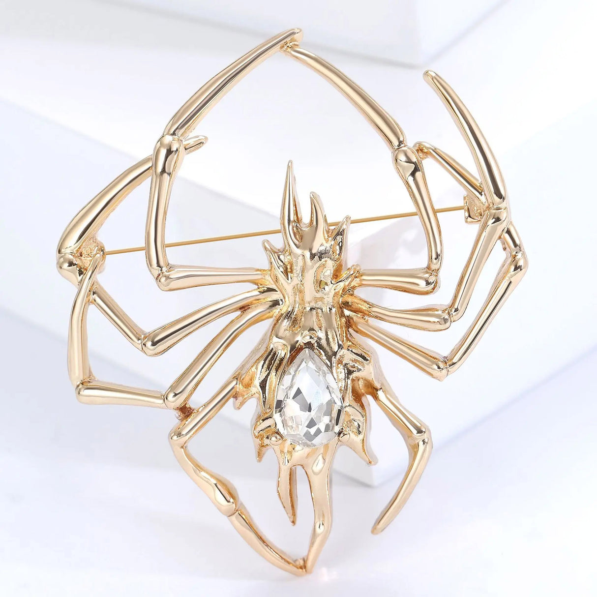 Studio view of gold-tone spider brooch with clear faceted center stone, upright pose on white display.