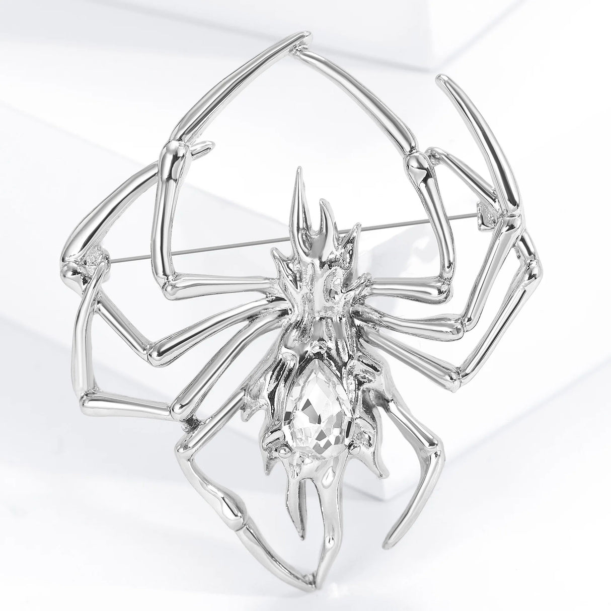 Silver-tone spider brooch with clear decorative center stone, upright studio shot.
