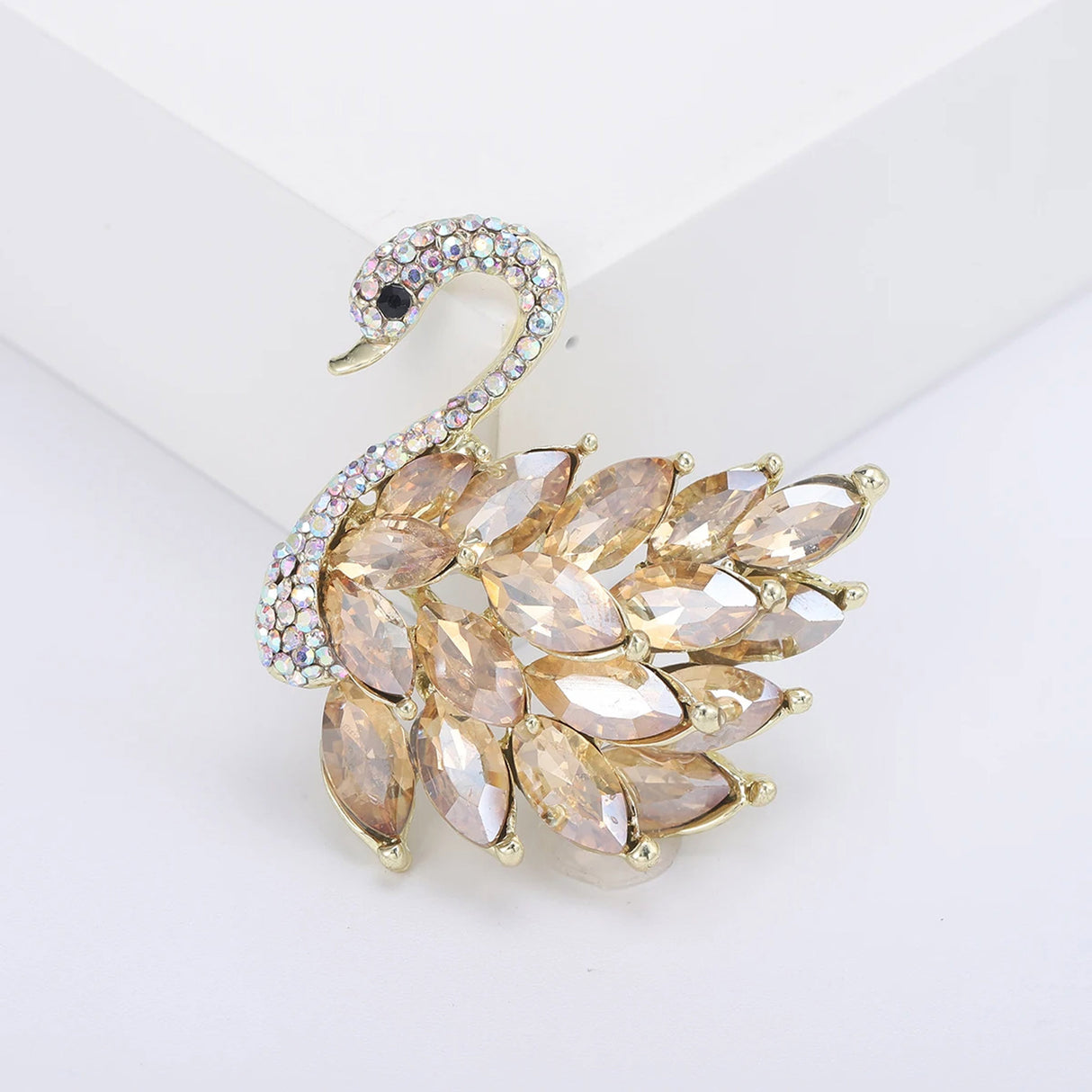 Swan brooch with gold-tone metal base, amber-colored marquise-cut faceted stones, and multicolor pavé head, front view in white studio setting.