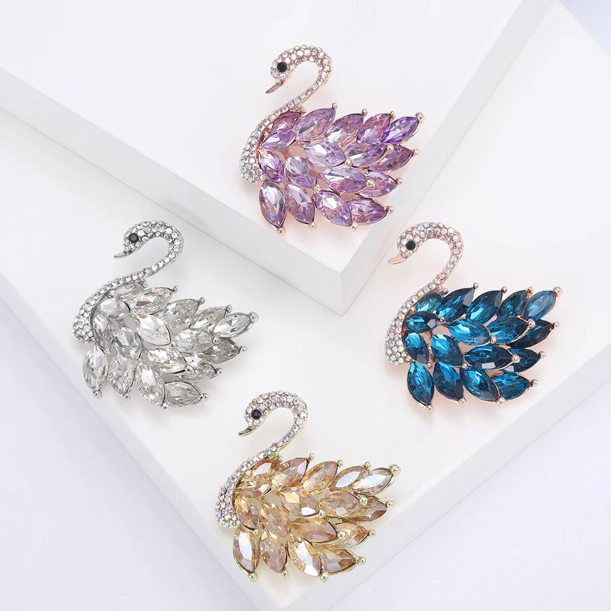 Set of four swan brooches with multicolor faceted stones in amber-yellow, blue, purple, and clear-white colors. Flat lay display.
