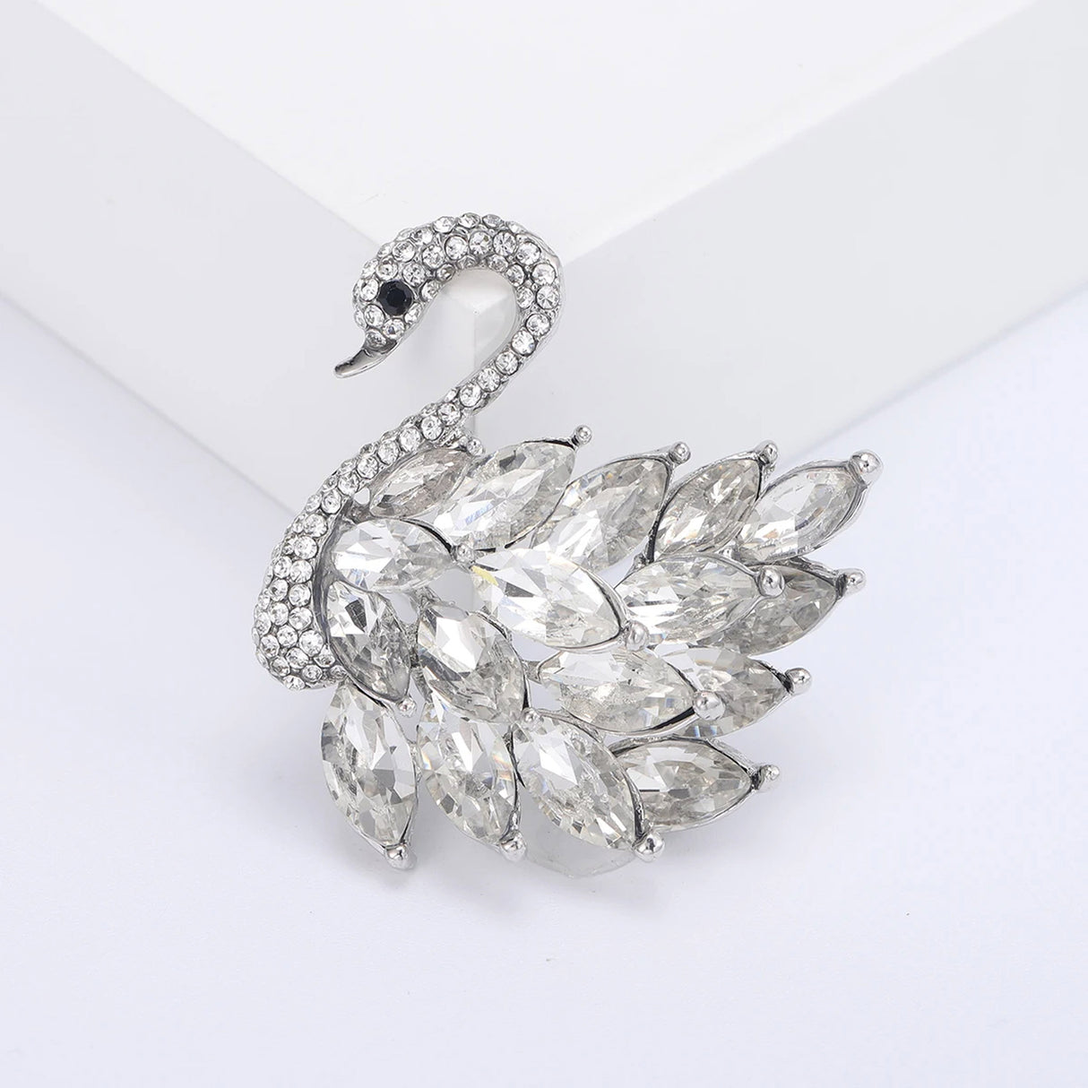 Swan brooch with silver-tone metal, clear marquise-cut faceted stones as feathers, and pavé head detail. Front view in white studio setting.