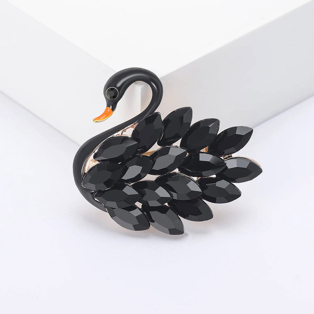 Swan brooch featuring glossy black body, black faceted stones, and orange beak, front view on white surface.