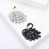 Pair of swan brooches with black and white enamel bodies and marquise-cut stones as feathers. Top-down view on white studio background.