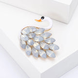 Swan brooch with white-tone body, orange beak, and white iridescent marquise-cut stones, angled view on white block.